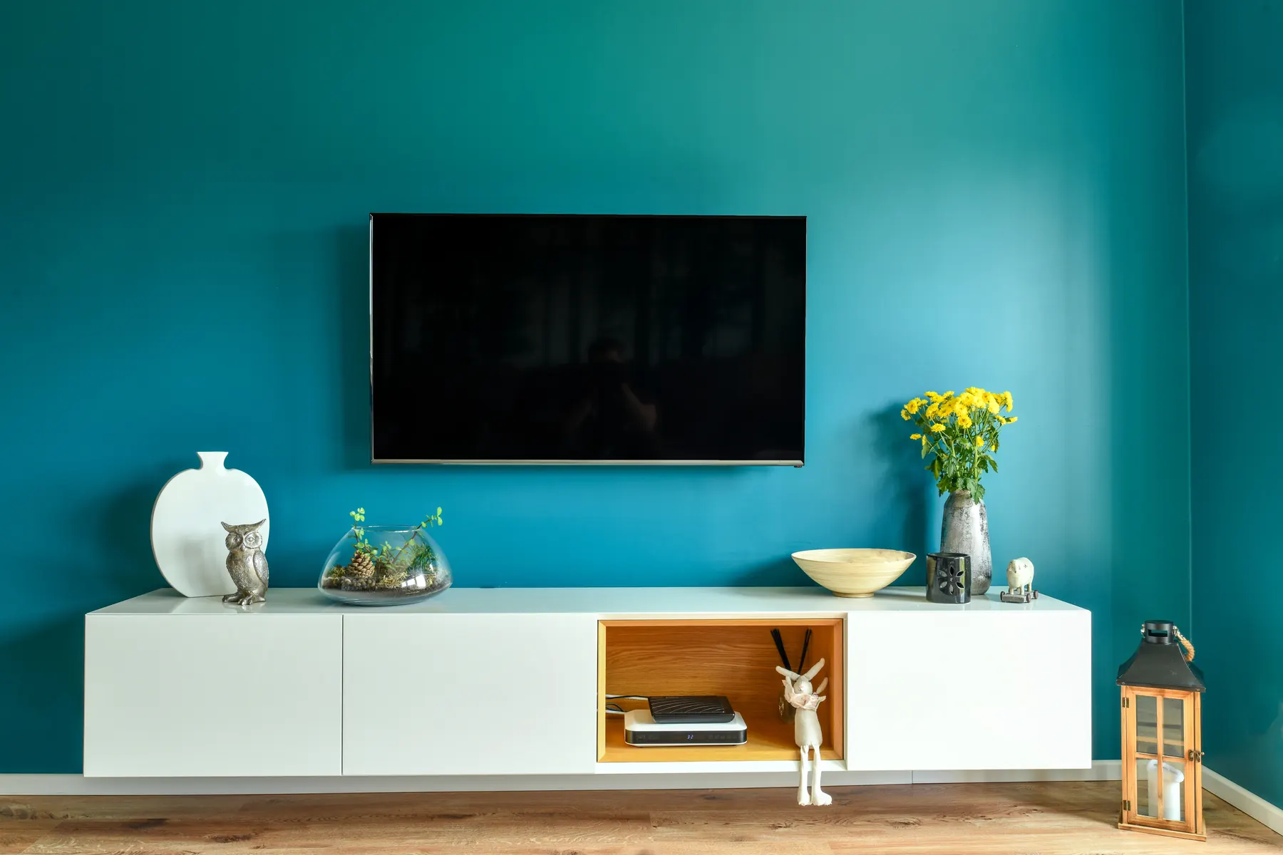 A television mounted flat against a teal painted wall above a white floating sideboard, with nothing running down the wall beneath it