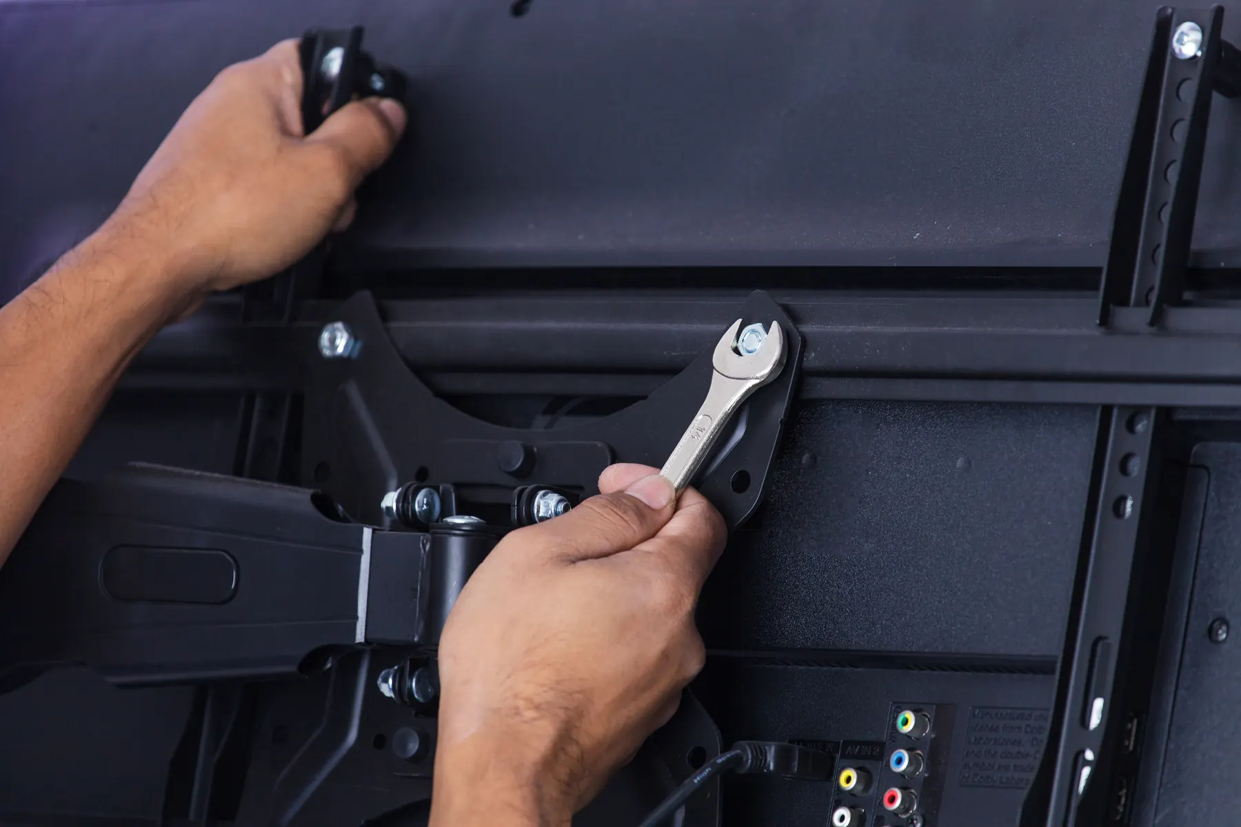 Close view of two hands tightening a bolt on an articulated mount arm behind a television