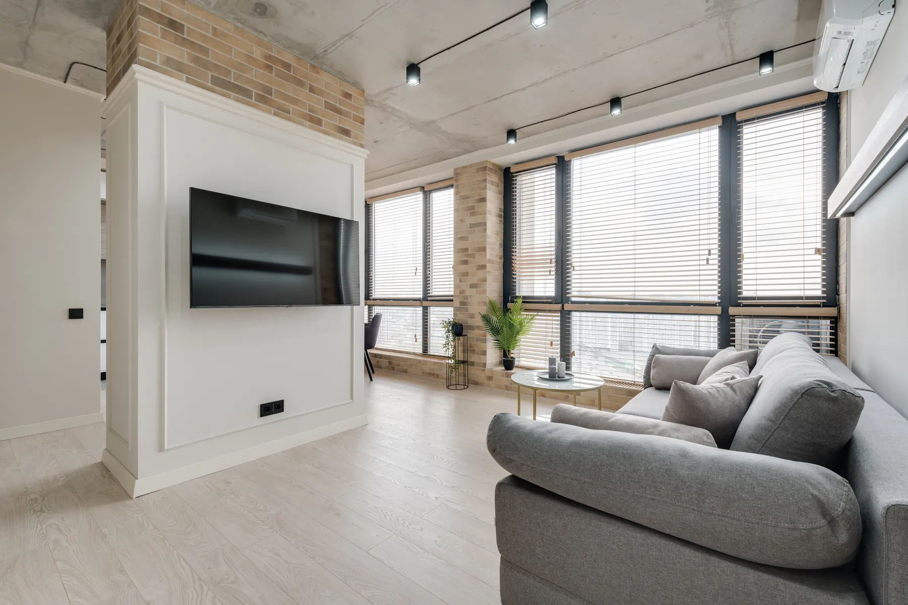 A television mounted on a white panelled chimney breast with pale brick above it in a loft style room